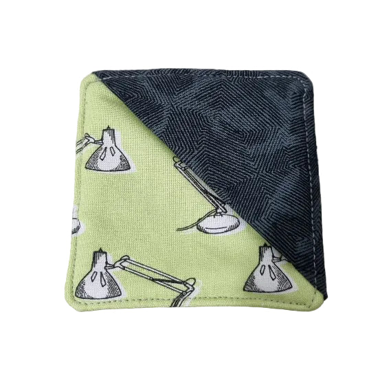A square fabric bookmark with a diagonal split design, featuring a light green side with a black-and-white lamp print and a dark charcoal gray side with a textured geometric pattern.