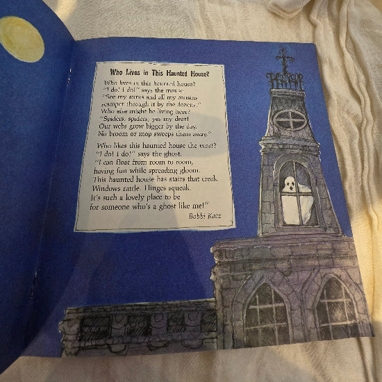 An open children's book showing a page with a poem titled "Who Lives in This Haunted House?" on a blue background, alongside an illustration of a haunted house and a ghost.