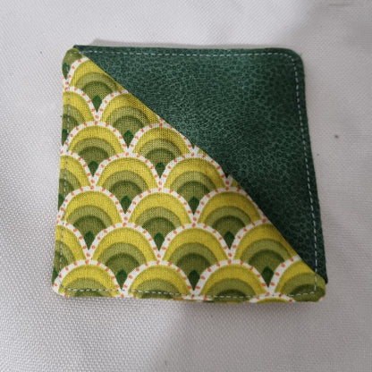 A square fabric bookmark. One half features a green textured leather-like finish, and the other half has a repeating scallop pattern in shades of green, yellow, and white.