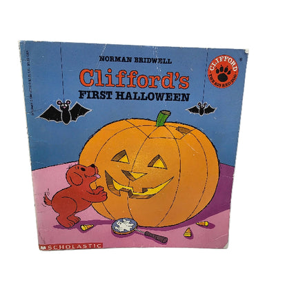 A vintage children's book titled 'Clifford's First Halloween' by Norman Bridwell, published by Scholastic. The cover features a cartoon illustration of a large orange jack-o'-lantern pumpkin, a small red dog , and a blue sky background with bats.